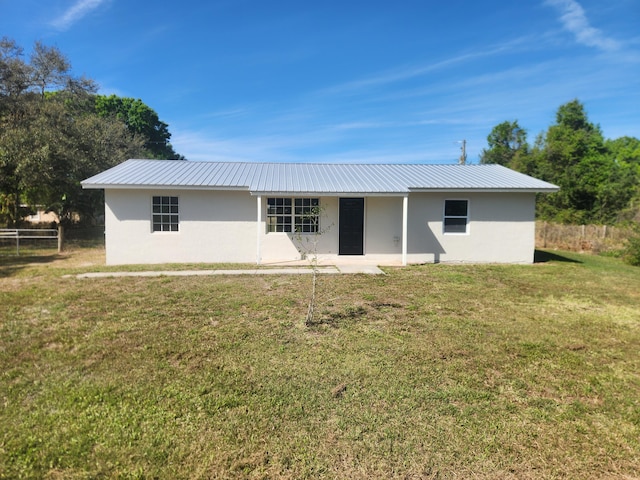 back of house featuring metal roof, a lawn, and stucco siding