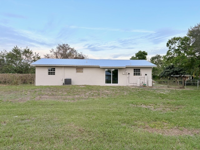 back of property with stucco siding, metal roof, central AC, and a yard