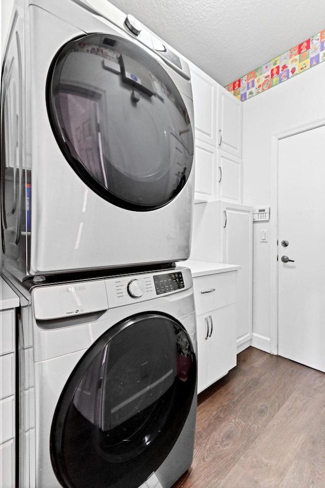 clothes washing area featuring stacked washer and dryer, a textured ceiling, dark wood-style floors, and cabinet space