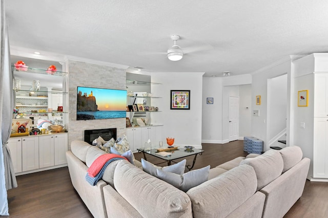 living area with dark wood-style flooring, a ceiling fan, ornamental molding, a large fireplace, and a textured ceiling