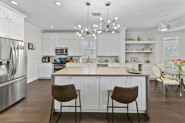 kitchen with a kitchen island, appliances with stainless steel finishes, white cabinets, and decorative light fixtures