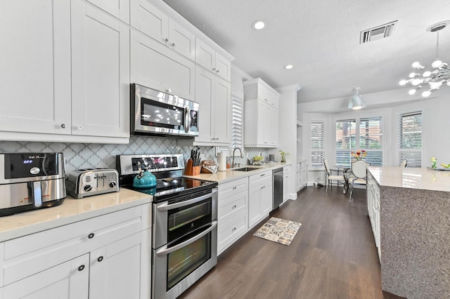 kitchen featuring stainless steel appliances, a sink, white cabinets, hanging light fixtures, and light countertops