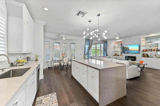 kitchen featuring a sink, white cabinets, open floor plan, hanging light fixtures, and a center island