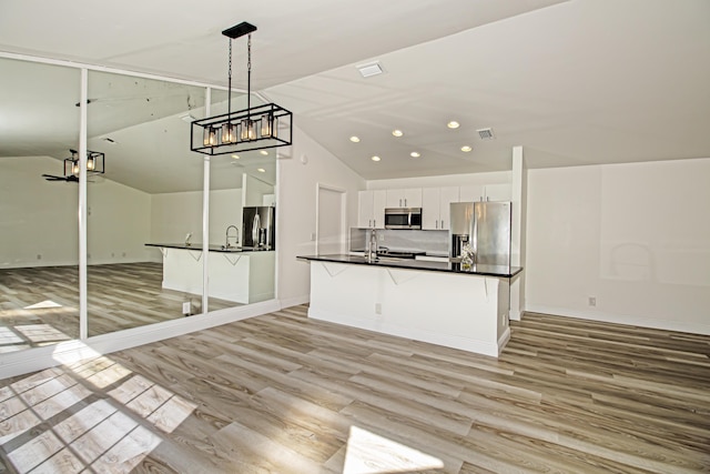 kitchen featuring a kitchen bar, vaulted ceiling, appliances with stainless steel finishes, pendant lighting, and white cabinets