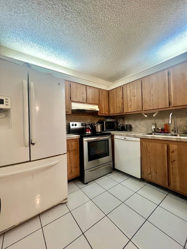 kitchen with tasteful backsplash, light countertops, appliances with stainless steel finishes, a sink, and under cabinet range hood