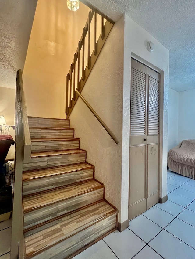 stairs featuring a textured wall, a textured ceiling, and tile patterned floors