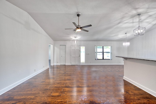 unfurnished living room featuring dark wood-style floors, vaulted ceiling, baseboards, and ceiling fan with notable chandelier