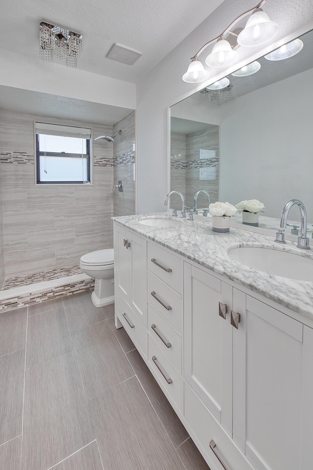 bathroom featuring toilet, double vanity, a walk in shower, and a sink