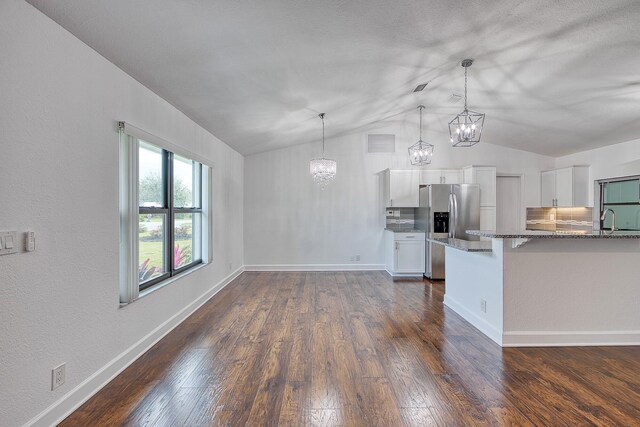 unfurnished living room with baseboards, visible vents, dark wood-style floors, vaulted ceiling, and ceiling fan with notable chandelier