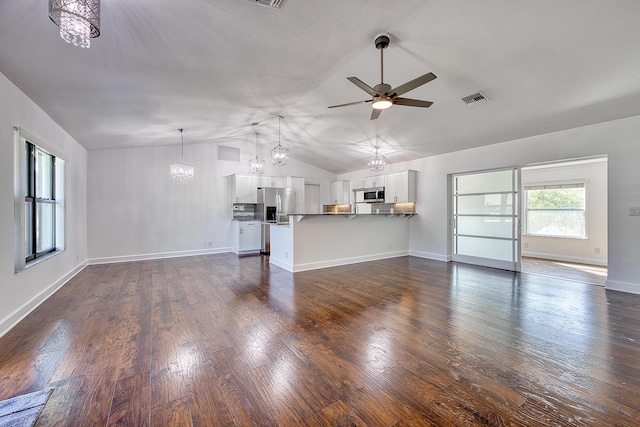 unfurnished living room with lofted ceiling, visible vents, dark wood finished floors, and ceiling fan with notable chandelier