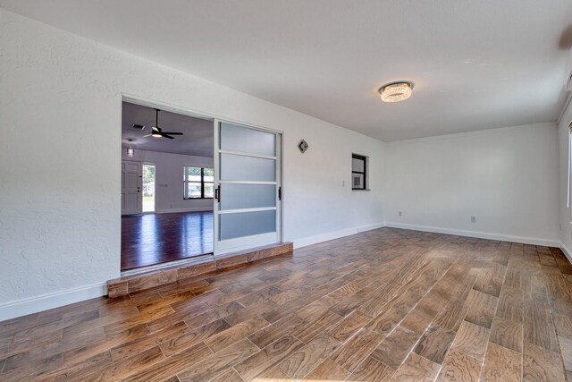 empty room featuring a chandelier, wood finished floors, baseboards, and a wall mounted AC