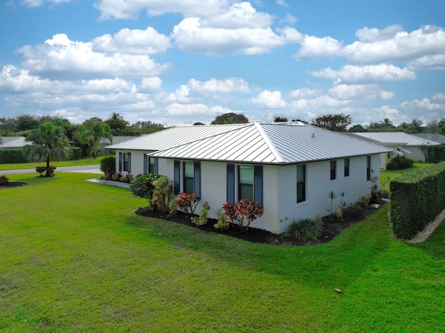 back of property featuring a standing seam roof, metal roof, a lawn, and stucco siding