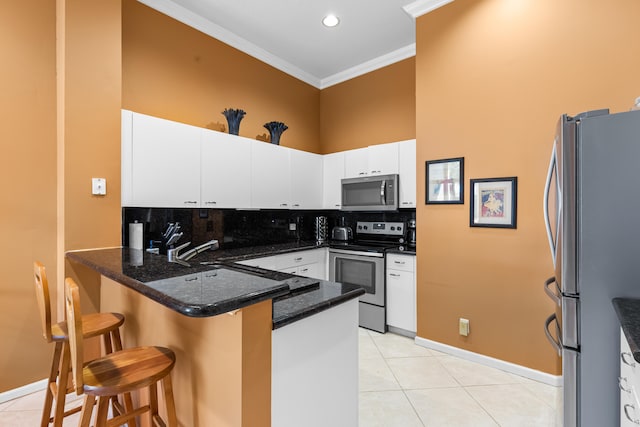 kitchen featuring ornamental molding, a kitchen breakfast bar, kitchen peninsula, stainless steel appliances, and white cabinets