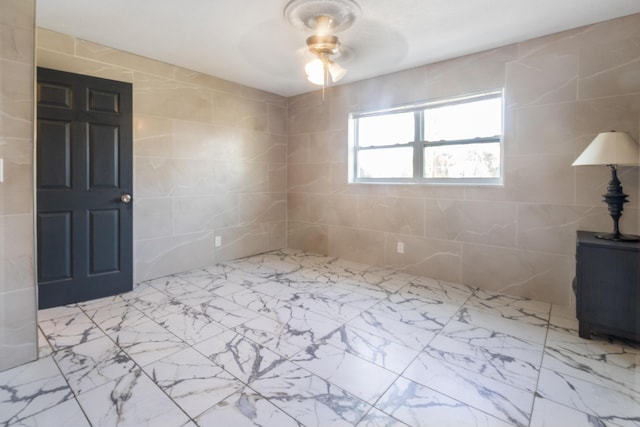 spare room featuring tile walls, ceiling fan, and marble finish floor