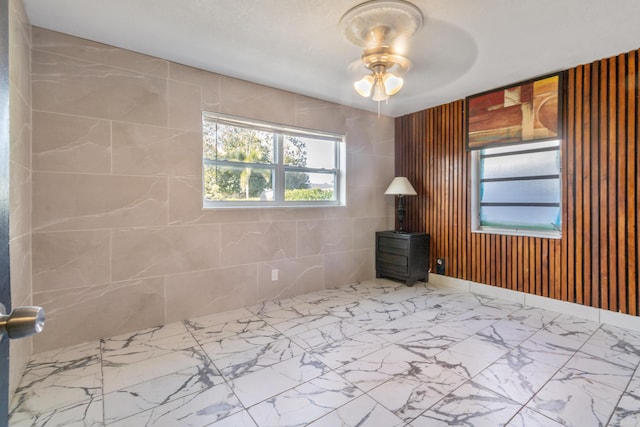 spare room with marble finish floor, a ceiling fan, tile walls, and a wood stove