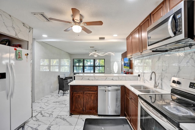 kitchen with a sink, marble finish floor, a peninsula, a ceiling fan, and stainless steel appliances
