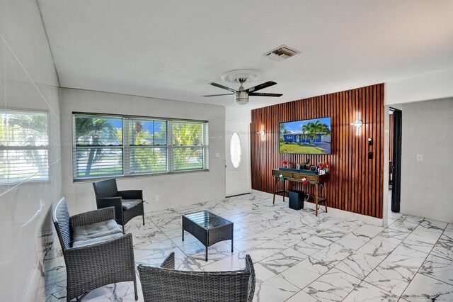 living area featuring wooden walls, ceiling fan, visible vents, and marble finish floor