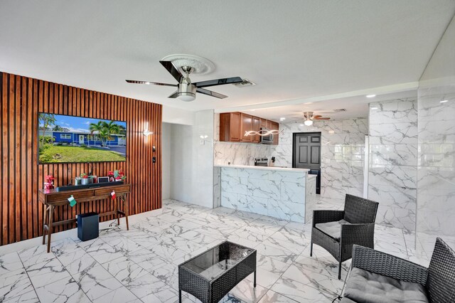 living area with a ceiling fan, tile walls, and marble finish floor