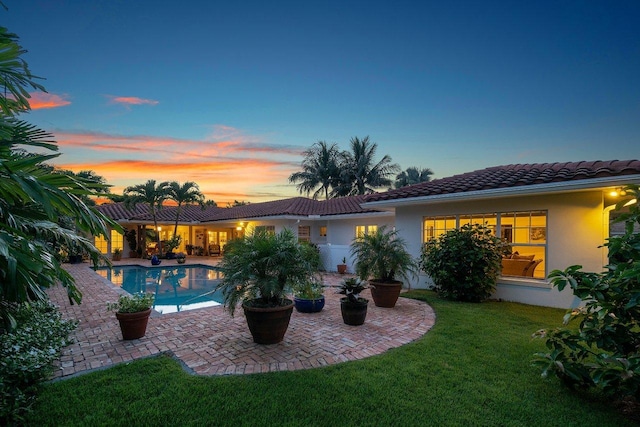 pool at dusk featuring a patio area and a lawn