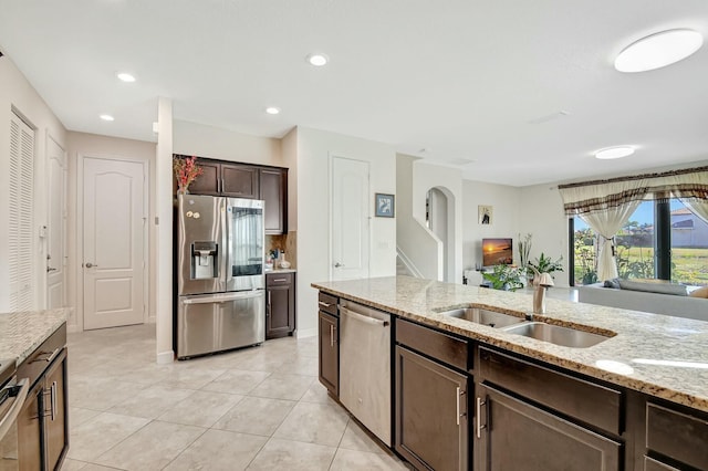 kitchen with dark brown cabinetry, sink, light stone counters, light tile patterned floors, and stainless steel appliances