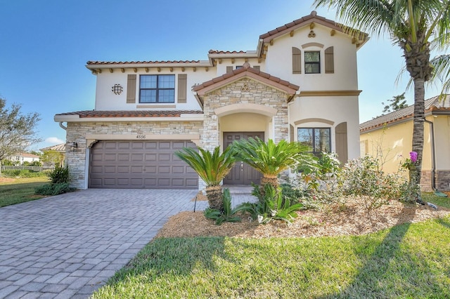 mediterranean / spanish-style house with stone siding, a tiled roof, an attached garage, decorative driveway, and stucco siding