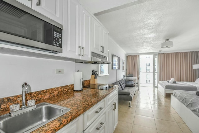 kitchen with sink, a textured ceiling, light tile patterned floors, black electric cooktop, and white cabinets