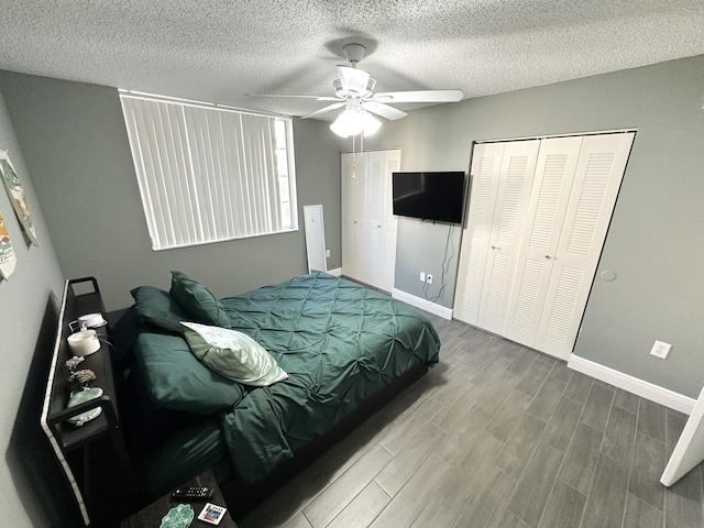 bedroom featuring hardwood / wood-style flooring, ceiling fan, multiple closets, and a textured ceiling