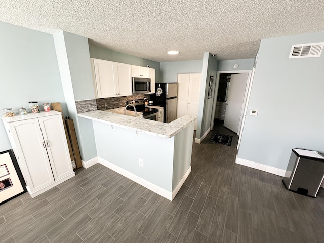 kitchen with appliances with stainless steel finishes, tasteful backsplash, a textured ceiling, white cabinets, and kitchen peninsula