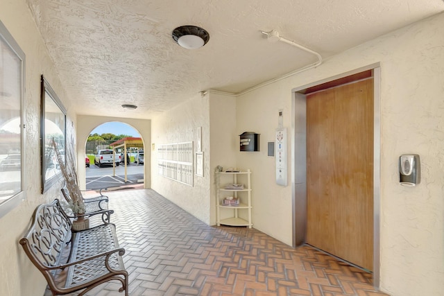 corridor with elevator and a textured ceiling