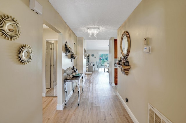 hallway featuring baseboards, visible vents, light wood-style floors, and a notable chandelier