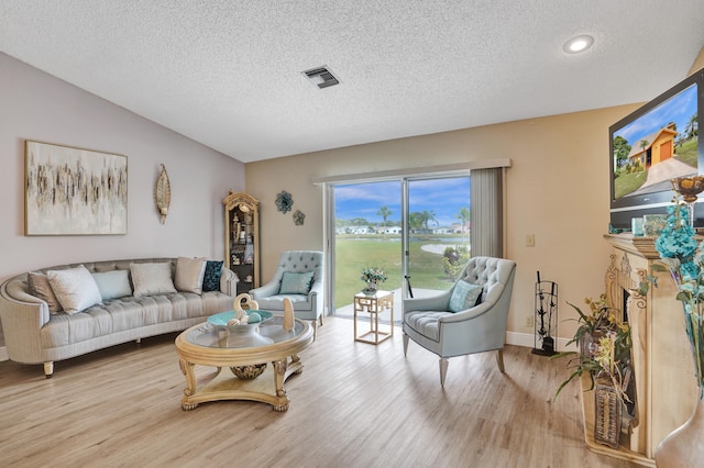 living room with a textured ceiling, light wood-type flooring, visible vents, and baseboards