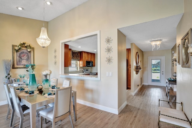 dining room with a textured ceiling, an inviting chandelier, and light wood-style floors