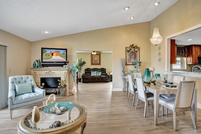 living room with a textured ceiling, a fireplace, baseboards, vaulted ceiling, and light wood-style floors