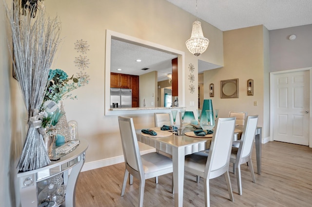 dining space with a textured ceiling, a chandelier, light wood-style flooring, and baseboards