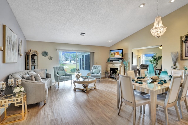 dining space featuring vaulted ceiling, visible vents, light wood-style flooring, a tiled fireplace, and a textured ceiling