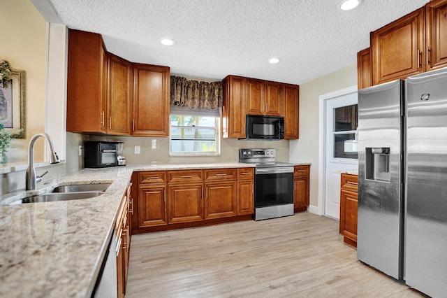 kitchen featuring stainless steel appliances, brown cabinetry, a sink, light wood-style flooring, and a textured ceiling