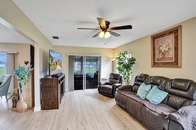 living room with ceiling fan, a textured ceiling, visible vents, light wood-style floors, and plenty of natural light