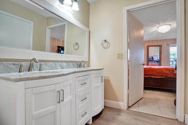 ensuite bathroom featuring wood finished floors, baseboards, a sink, and double vanity