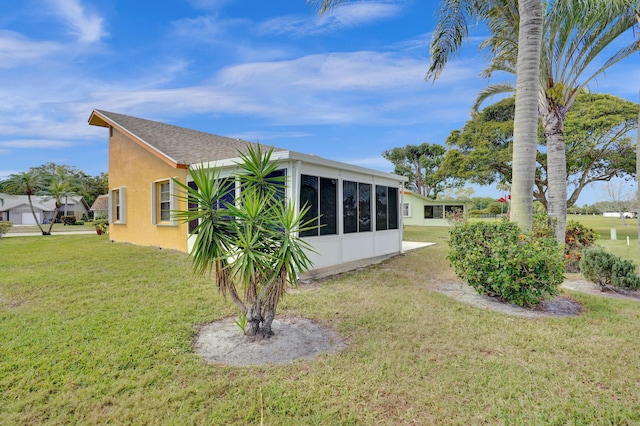 back of house with stucco siding, a shingled roof, a sunroom, and a yard