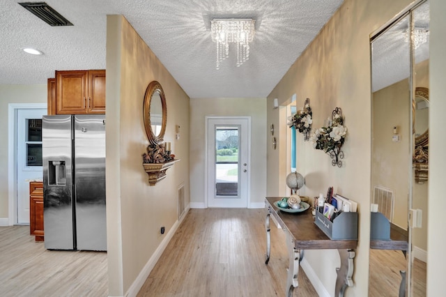 doorway to outside with baseboards, visible vents, light wood-style flooring, and a textured ceiling