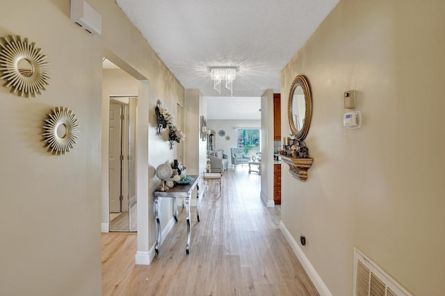 hall with light wood-style floors, baseboards, visible vents, and a textured ceiling