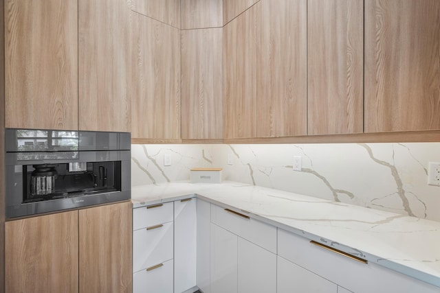 kitchen with tasteful backsplash, white cabinets, wall oven, light stone counters, and light brown cabinets