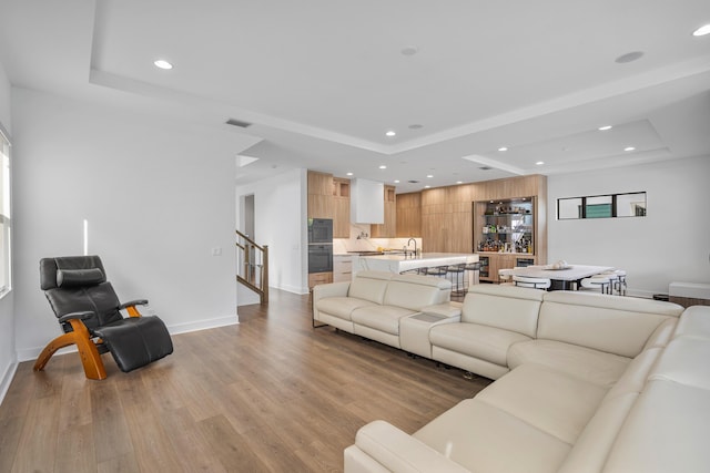 living room featuring sink, a raised ceiling, and light hardwood / wood-style floors