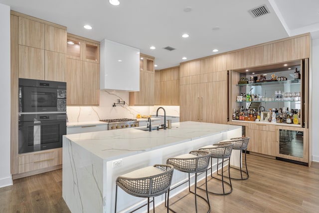 kitchen with a kitchen island with sink, light stone counters, beverage cooler, and a kitchen bar