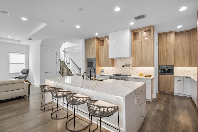 kitchen with sink, a kitchen island with sink, light stone counters, white cabinets, and a kitchen bar