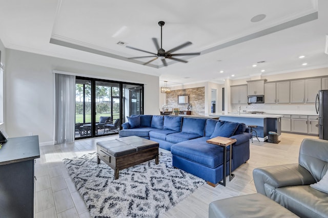 living room with a tray ceiling, light hardwood / wood-style flooring, ornamental molding, and ceiling fan