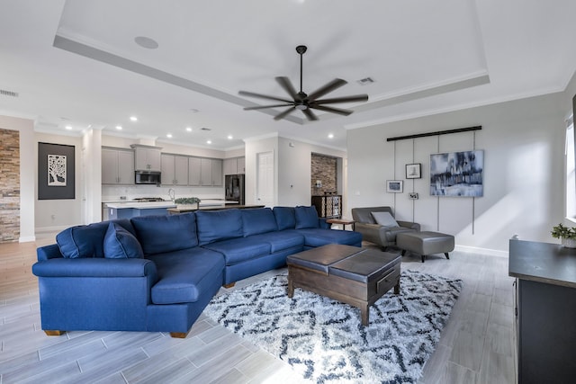 living room featuring ornamental molding, ceiling fan, light wood-type flooring, and a tray ceiling