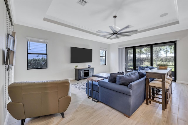 living room with a raised ceiling, ornamental molding, and a healthy amount of sunlight