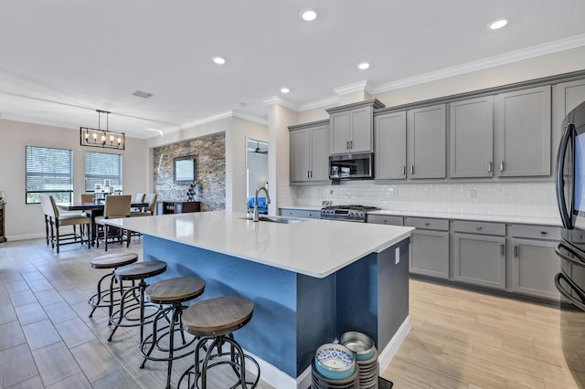 kitchen featuring appliances with stainless steel finishes, decorative light fixtures, sink, a breakfast bar area, and a kitchen island with sink