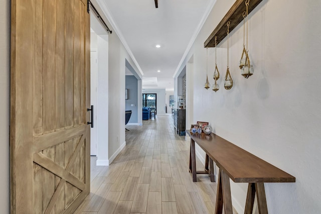 hall with ornamental molding, a barn door, and light wood-type flooring